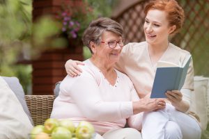 Idosa lendo com um cuidador de idosos profissional em um banco no jardim